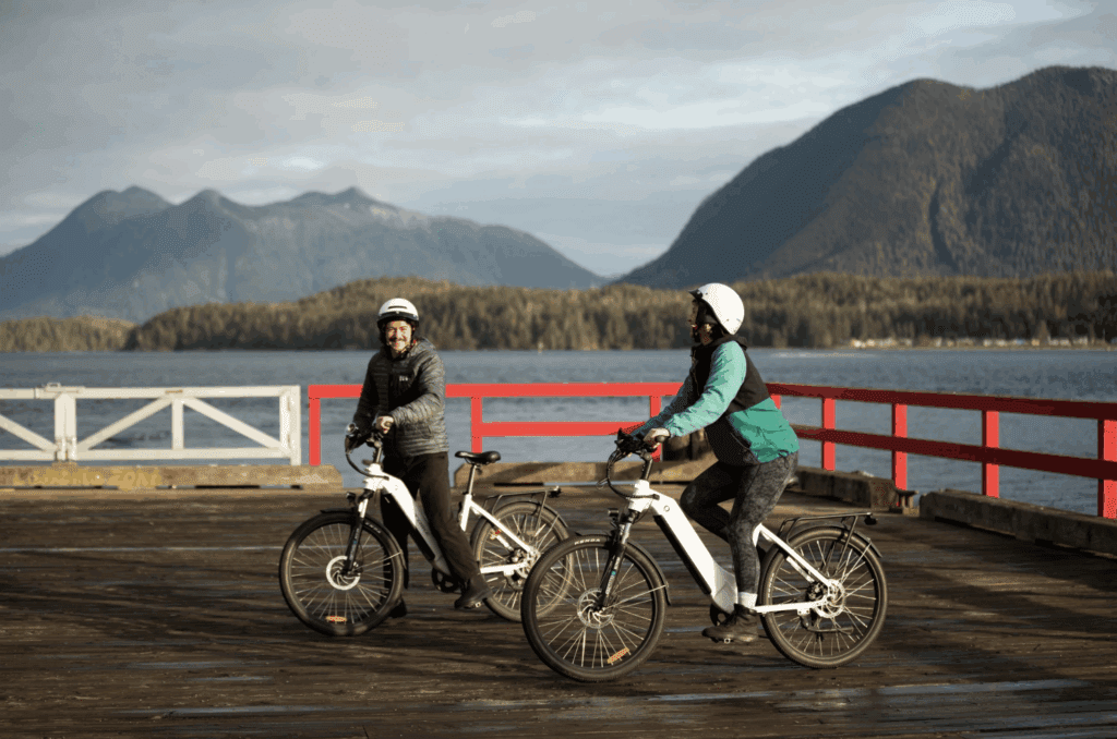 two people bike along a pier with mounains across a body of water