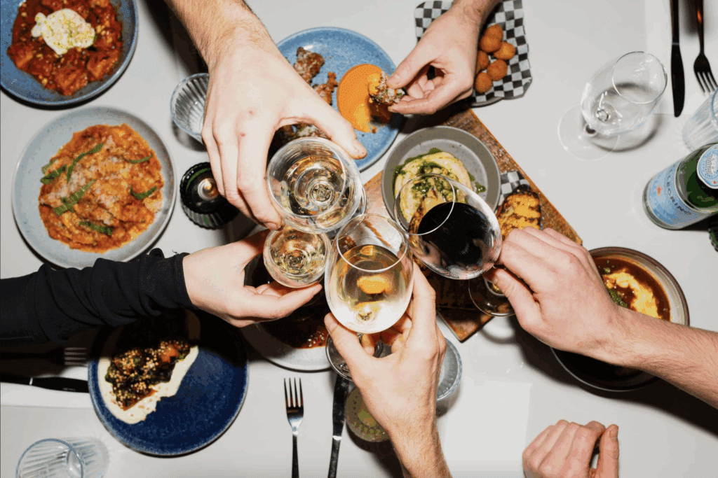 a funky photo of hands holding wine glasses with small plates on the table at Alfred's restaurant in Revelstoke