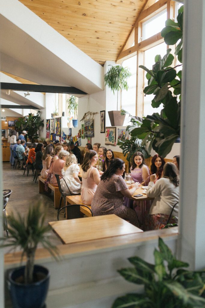 wedding guests at a long table in a restaurant with high ceilings and large plants
