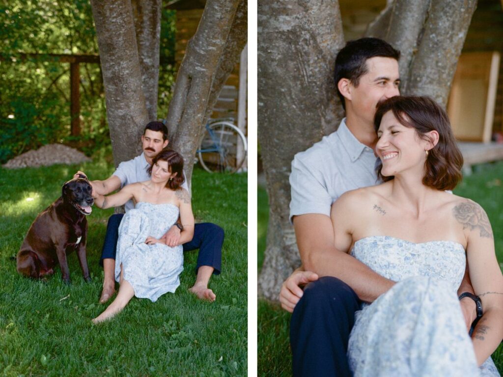 man and woman cuddle beside a tree
