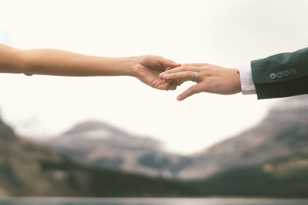 close up photo of a bride and groom's hands and their wedding rings set again a mountain backdrop