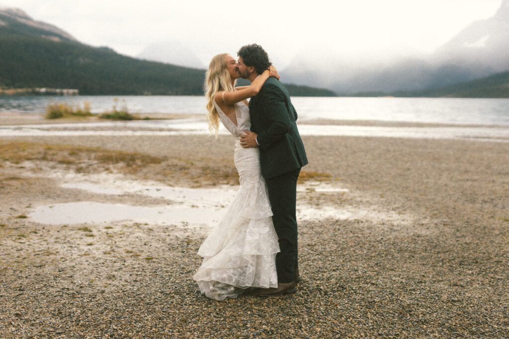 bride and groom kiss beside a mountain lake in Banff