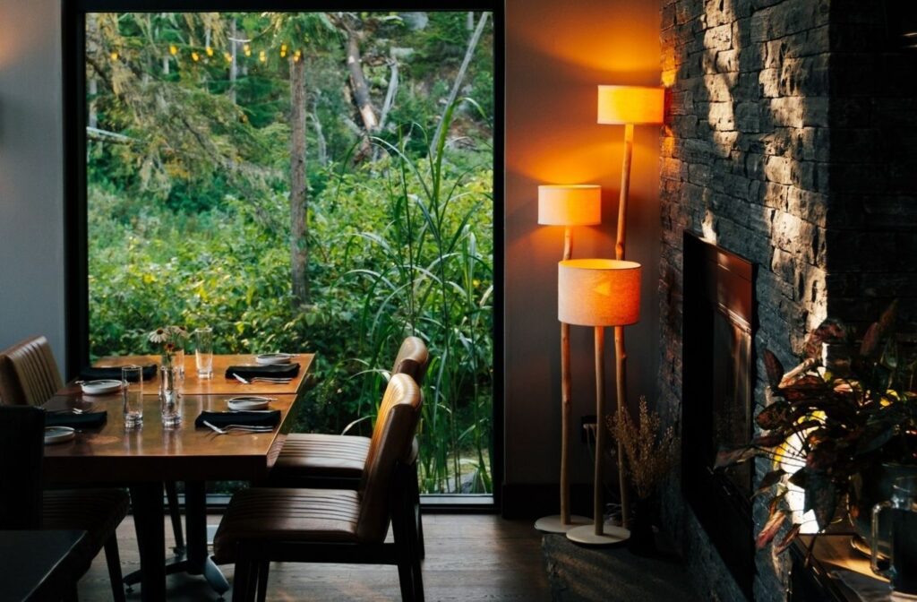 dining room in The Nest restaurant in Revelstoke - a modern space with dense foliage outside large windows and cozy ambient lighting indoors