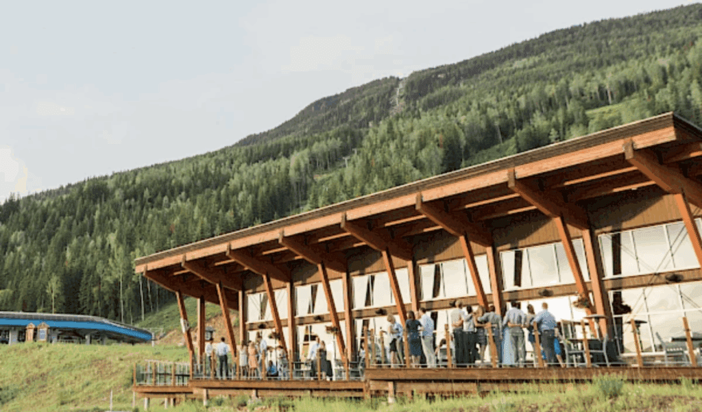 view from the outside of Revelation Lodge at Revelstoke Mountain Resort in summer with wedding guests milling about on the deck