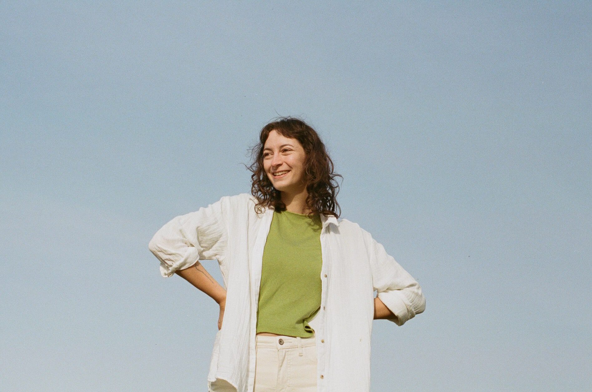 Revelstoke wedding photographer Heather Nolan stands with their arms stretched out in a loose linen shirt with a smile on their face