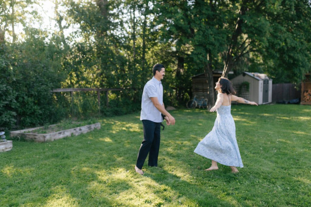 man and woman dressed in blue twirl in a backyard with dappled light