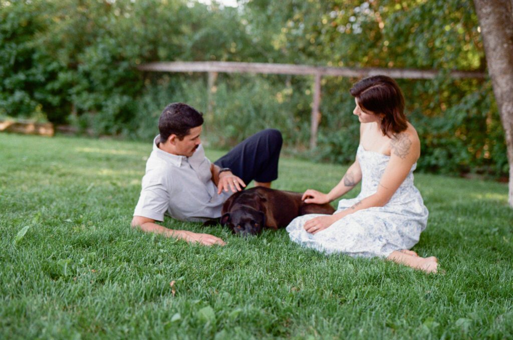 man and woman lie in the grass with their dog