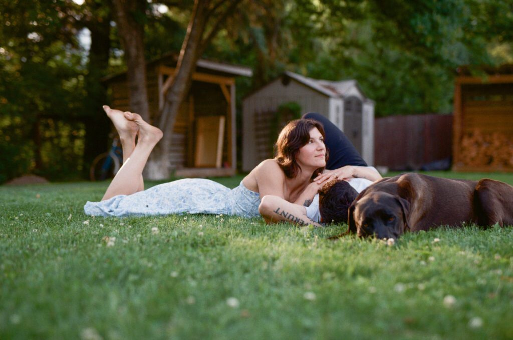 woman lies on man's chest in the grass, with their dog lying beside them