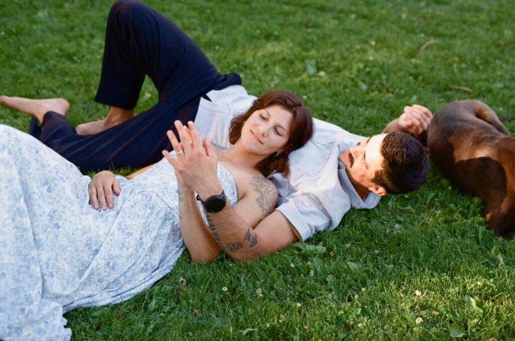 woman lies on man's chest in the grass, with their dog lying beside them