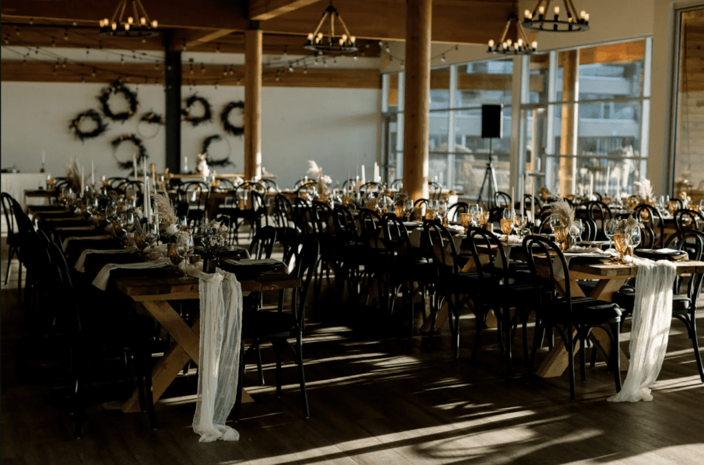 long dinner tables are set up for a wedding in a room with wooden beams and sunlight in Tofino, BC