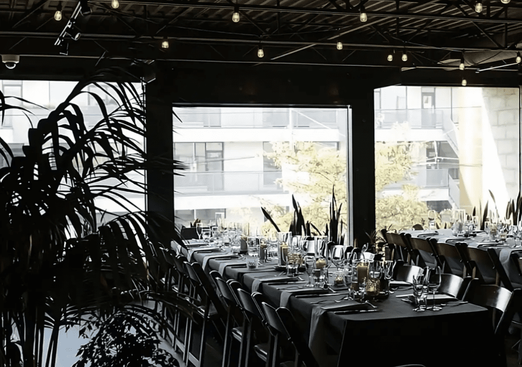 brightly lit interior set with long tables for a wedding with huge plants and edison bulbs in downtown Vancouver