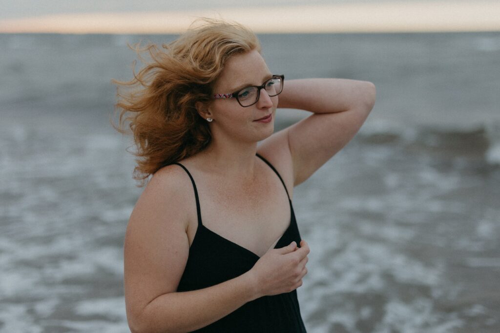 woman in a black dress stands on the seashore with a calm expression during Self Love Session on Vancouver Island