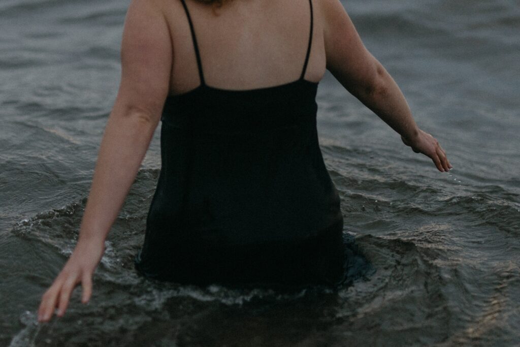 woman in a black dress wades hip-deep into the ocean at dusk during Self Love Session on Vancouver Island
